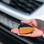 A hand holding a car key near a vehicle
