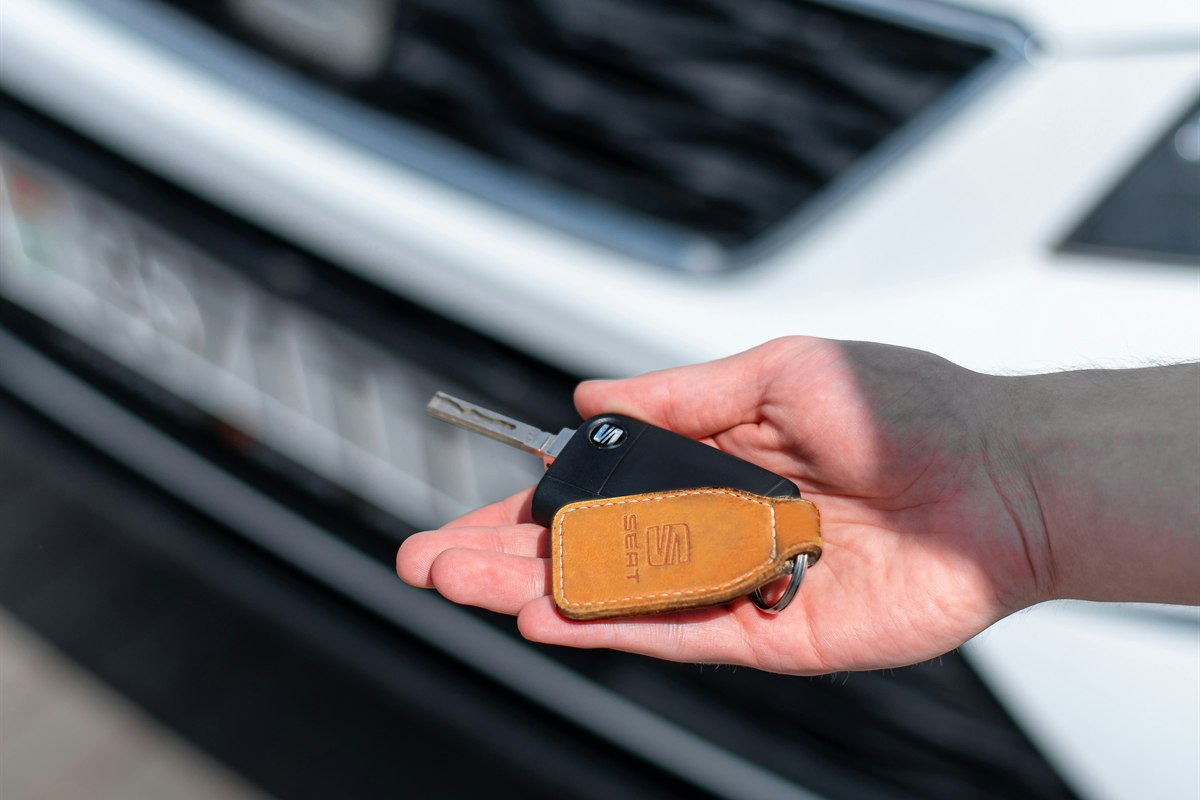 A hand holding a car key near a vehicle